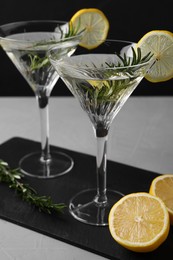 Martini glasses of refreshing cocktail decorated with lemon slices and rosemary on grey textured table