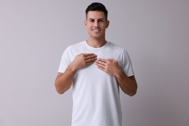 Photo of Handsome man holding hands near chest on grey background