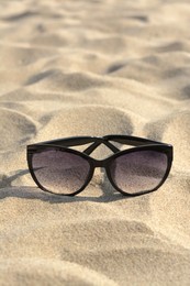 Stylish sunglasses with black frame on sandy beach