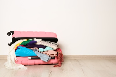 Suitcase with clothes for winter vacation on floor against white wall. Space for text