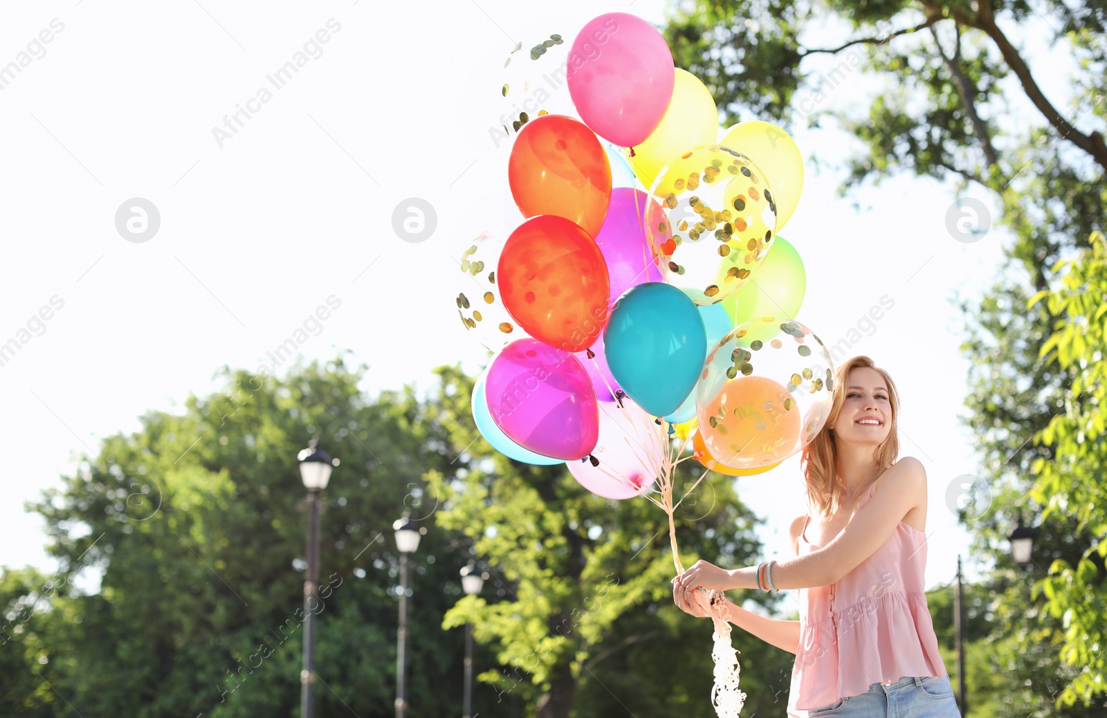 Photo of Young woman with colorful balloons outdoors on sunny day