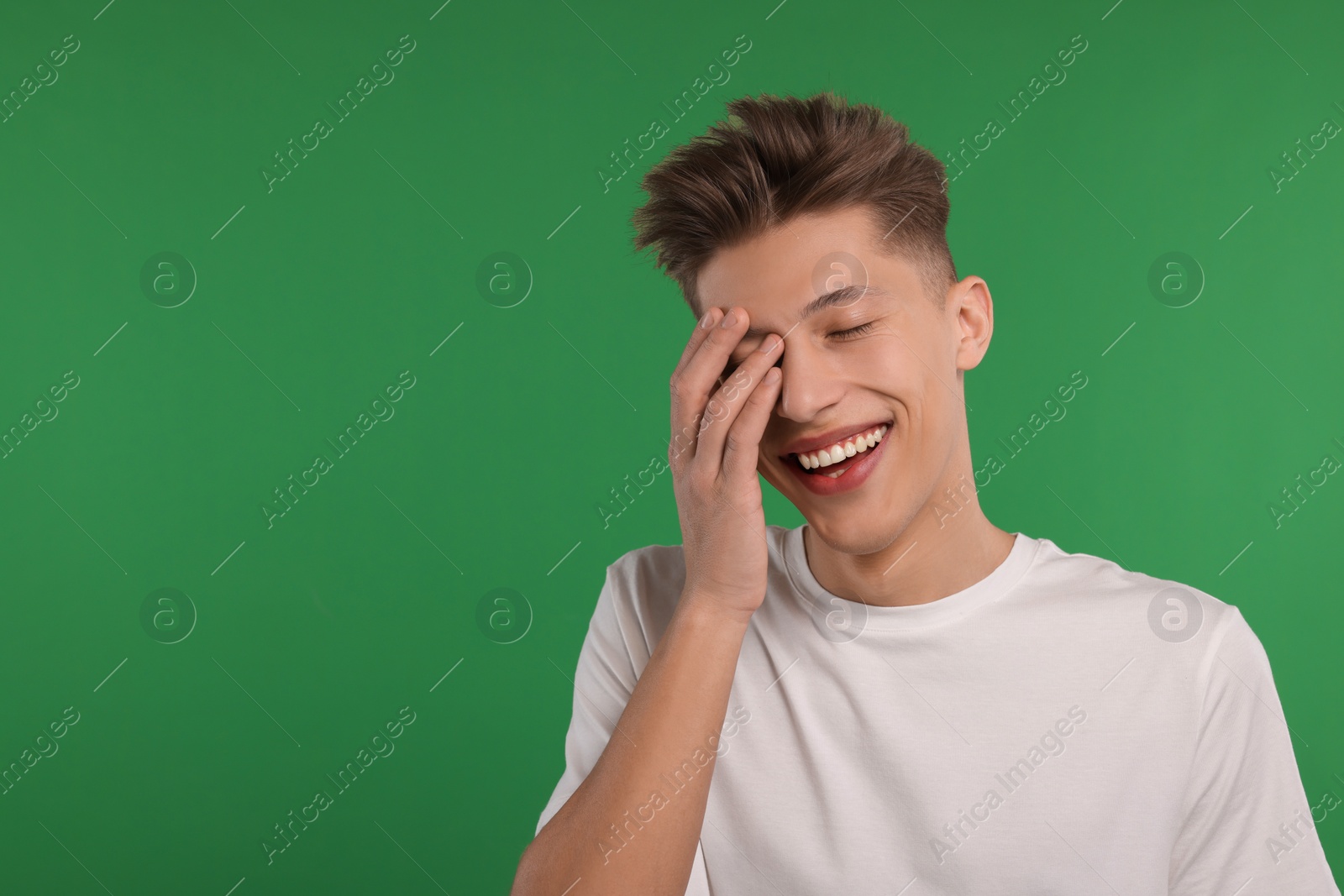 Photo of Portrait of young man laughing on green background. Space for text