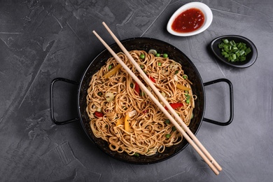 Photo of Cooked noodles with vegetables served on grey table, flat lay