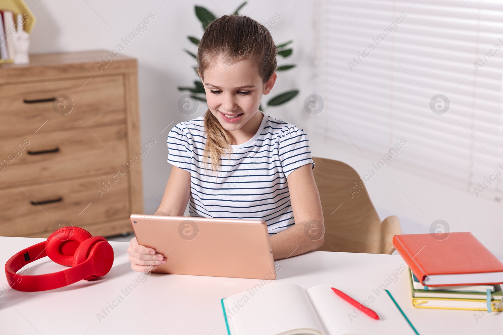 Photo of E-learning. Cute girl using tablet for studying online at table indoors