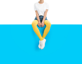 Photo of Woman wearing yellow tights and stylish shoes sitting on color background, closeup