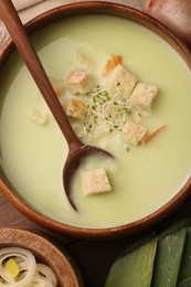 Bowl of tasty leek soup with croutons on wooden table, top view
