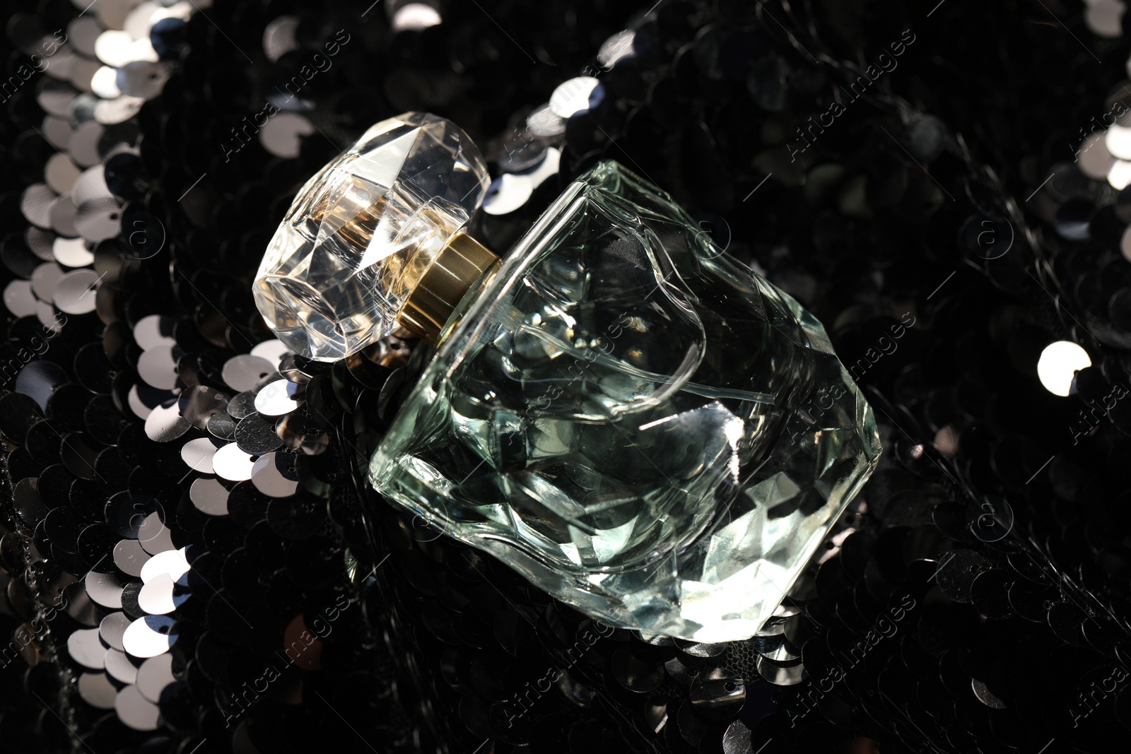 Photo of Luxury perfume in bottle on fabric with shiny sequins, closeup