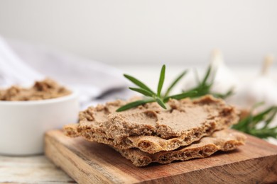 Photo of Crispy crackers with delicious meat pate and rosemary on wooden board, closeup