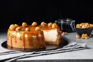 Sliced delicious cheesecake with caramel and popcorn on light grey table, space for text