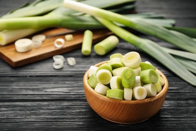 Cut fresh raw leek in bowl on black wooden table, space for text