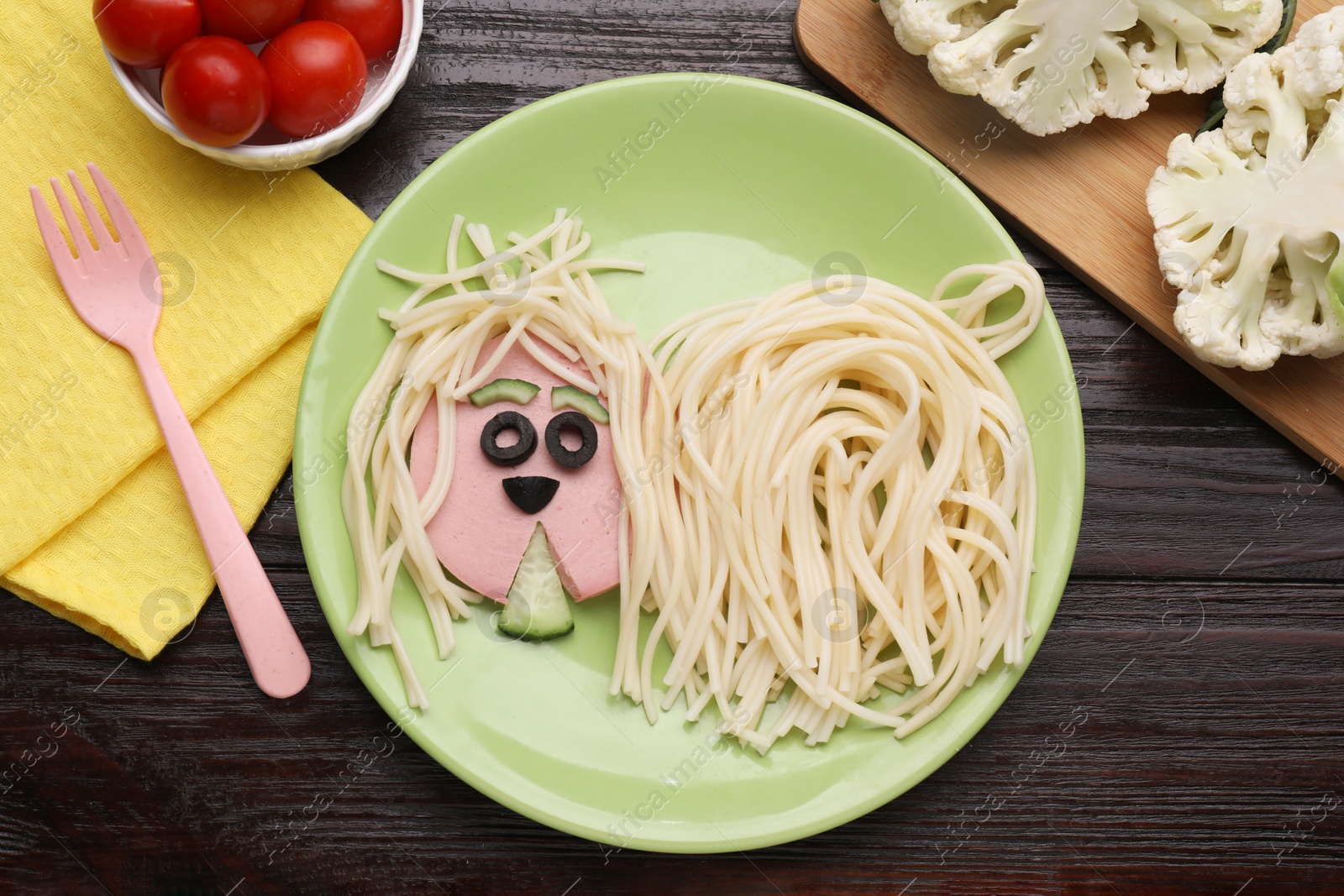 Photo of Creative serving for kids. Plate with cute dog made of tasty pasta, sausage and cucumber on wooden table, flat lay