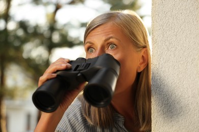 Photo of Concept of private life. Curious senior woman with binoculars spying on neighbours outdoors