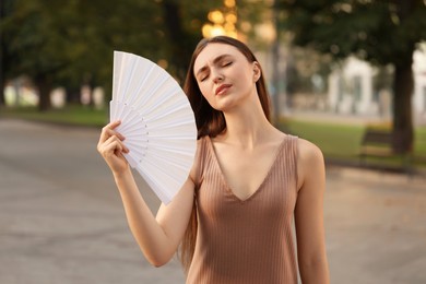 Woman with hand fan suffering from heat outdoors