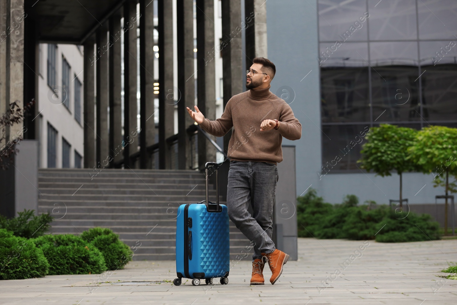 Photo of Being late. Worried man with suitcase near building outdoors