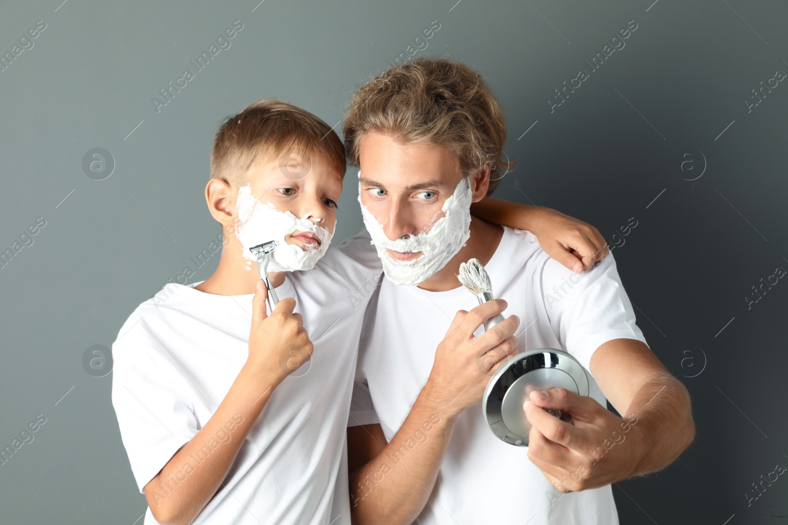 Photo of Father and son shaving together on color background
