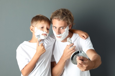 Photo of Father and son shaving together on color background