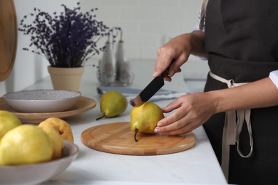 Photo of Woman cutting fresh ripe pear at table in kitchen, closeup