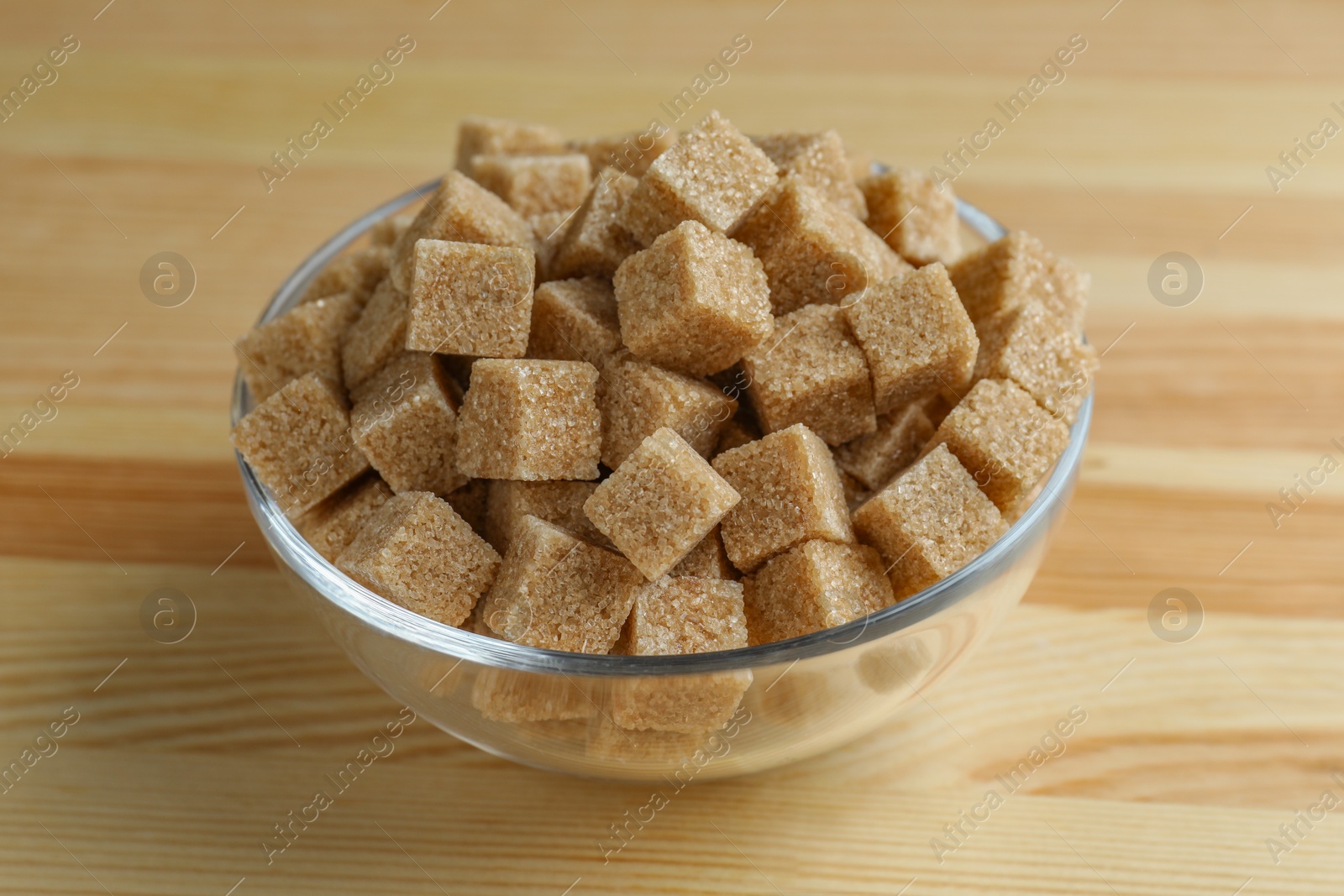 Photo of Brown sugar cubes in bowl on wooden table, closeup