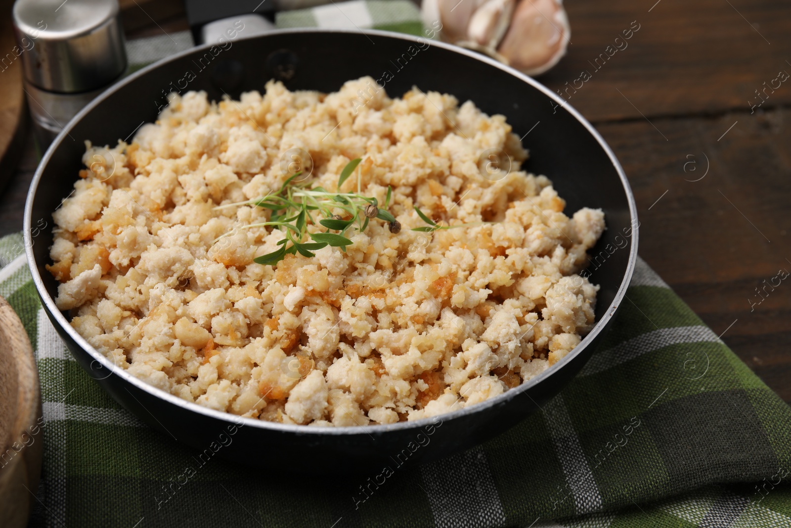 Photo of Fried ground meat in frying pan and microgreens on wooden table, closeup