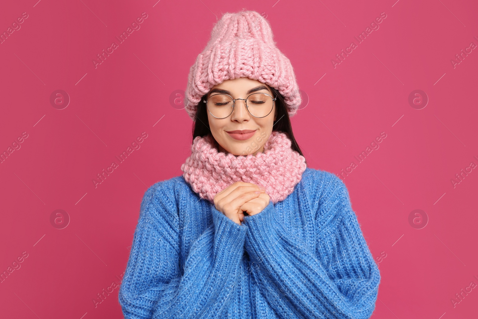 Photo of Young woman wearing warm sweater, snood and hat on crimson background. Winter season