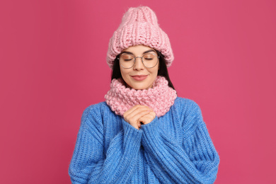 Young woman wearing warm sweater, snood and hat on crimson background. Winter season