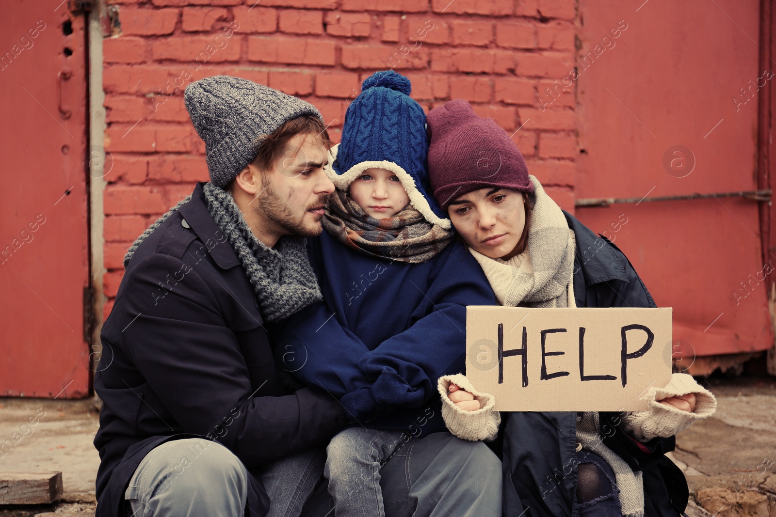 Photo of Poor young family with HELP sign on dirty street