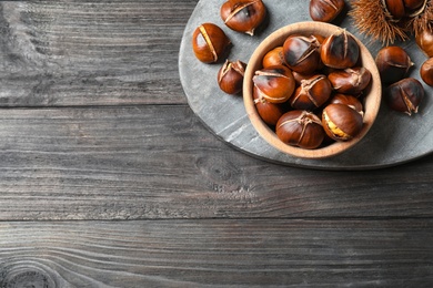 Photo of Delicious roasted edible chestnuts on black wooden table, top view. Space for text
