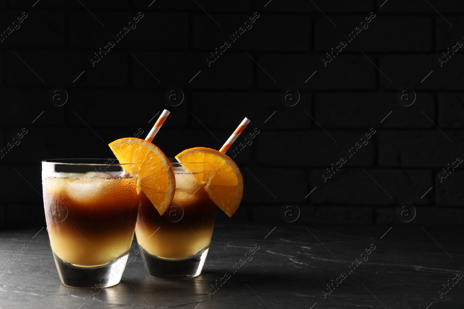 Photo of Tasty refreshing drink with coffee and orange juice on grey table against dark background, space for text