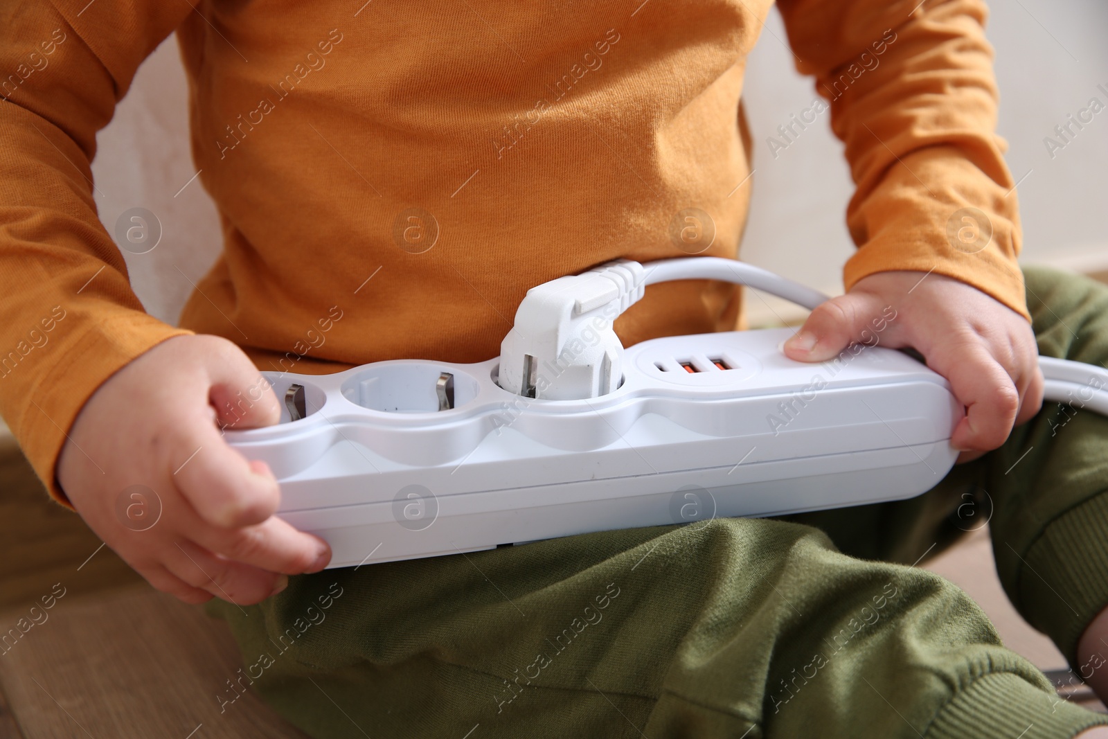 Photo of Little child playing with power strip and plug indoors, closeup