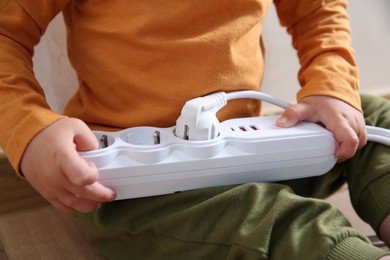 Little child playing with power strip and plug indoors, closeup