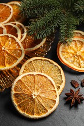 Photo of Dry orange slices, anise stars and fir tree branches on black table, closeup