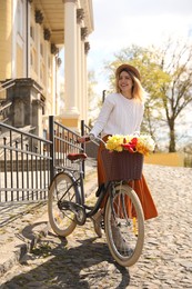 Beautiful young woman with bicycle and flowers on street