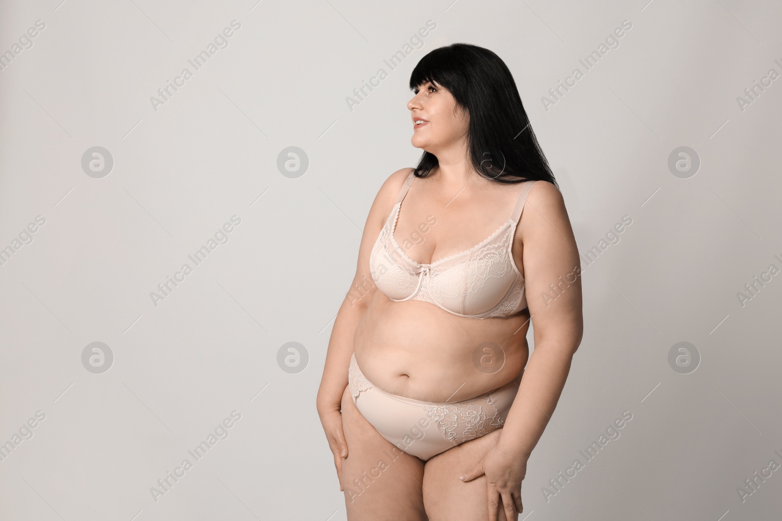 Photo of Beautiful overweight woman in beige underwear on light background, space for text. Plus-size model