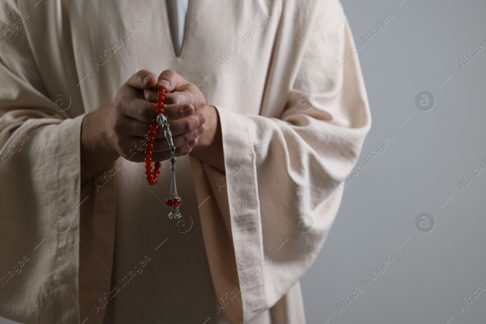 Photo of Muslim man with misbaha praying on light grey background, closeup. Space for text