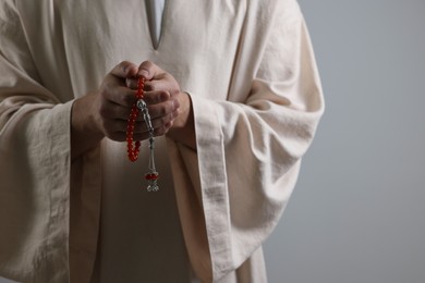 Muslim man with misbaha praying on light grey background, closeup. Space for text