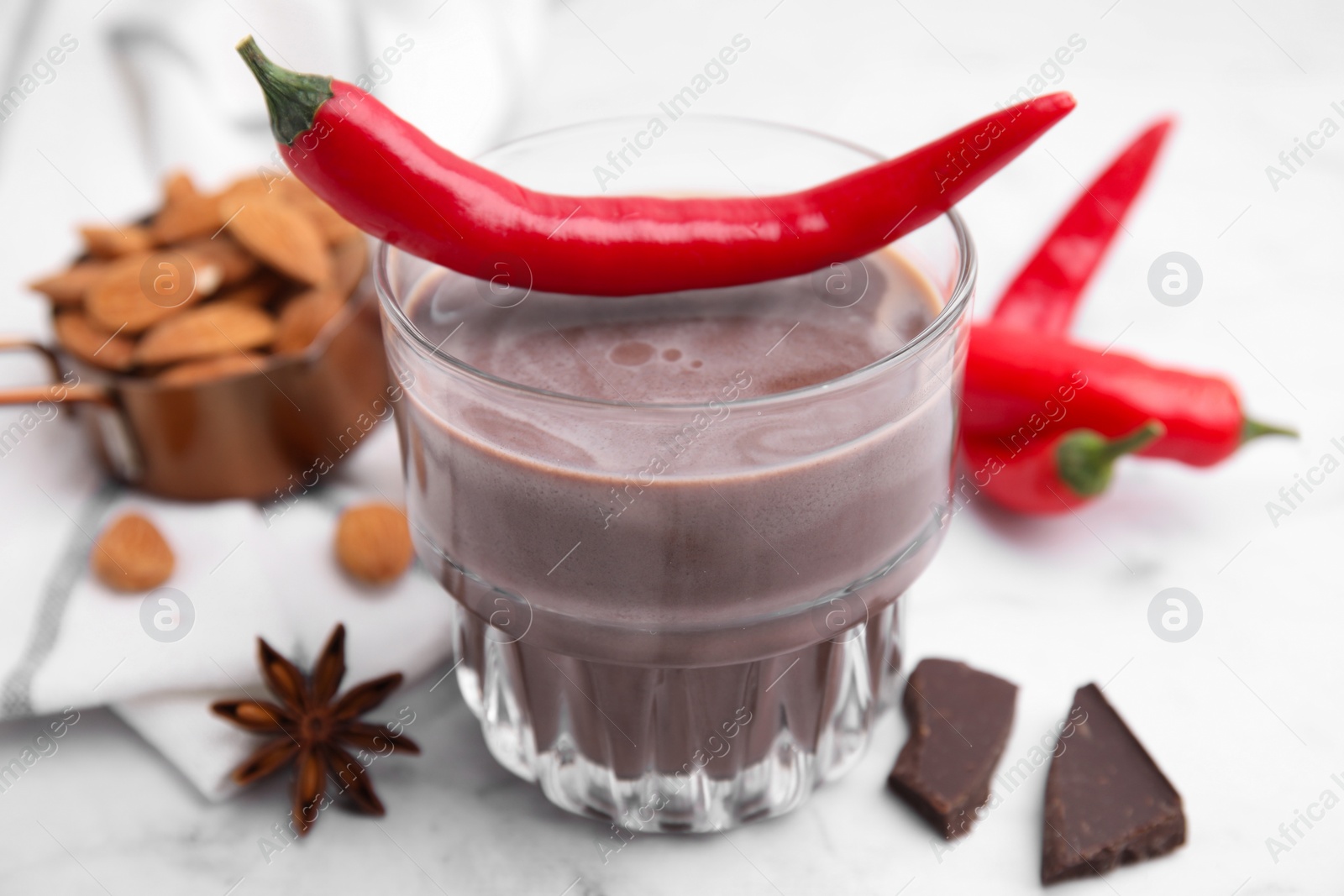 Photo of Glass of hot chocolate with chili pepper on white marble table, closeup