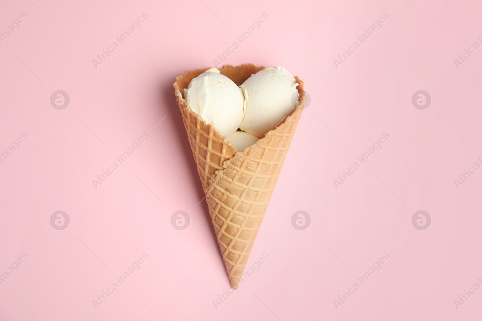 Photo of Delicious vanilla ice cream in wafer cone on pink background, top view