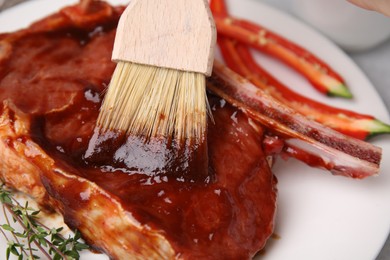 Photo of Spreading marinade onto raw meat with basting brush on table, closeup