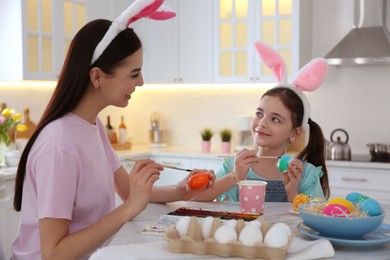 Photo of Happy mother with her cute daughter painting Easter eggs at table in kitchen