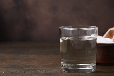 Photo of Vinegar in glass and baking soda on wooden table, space for text