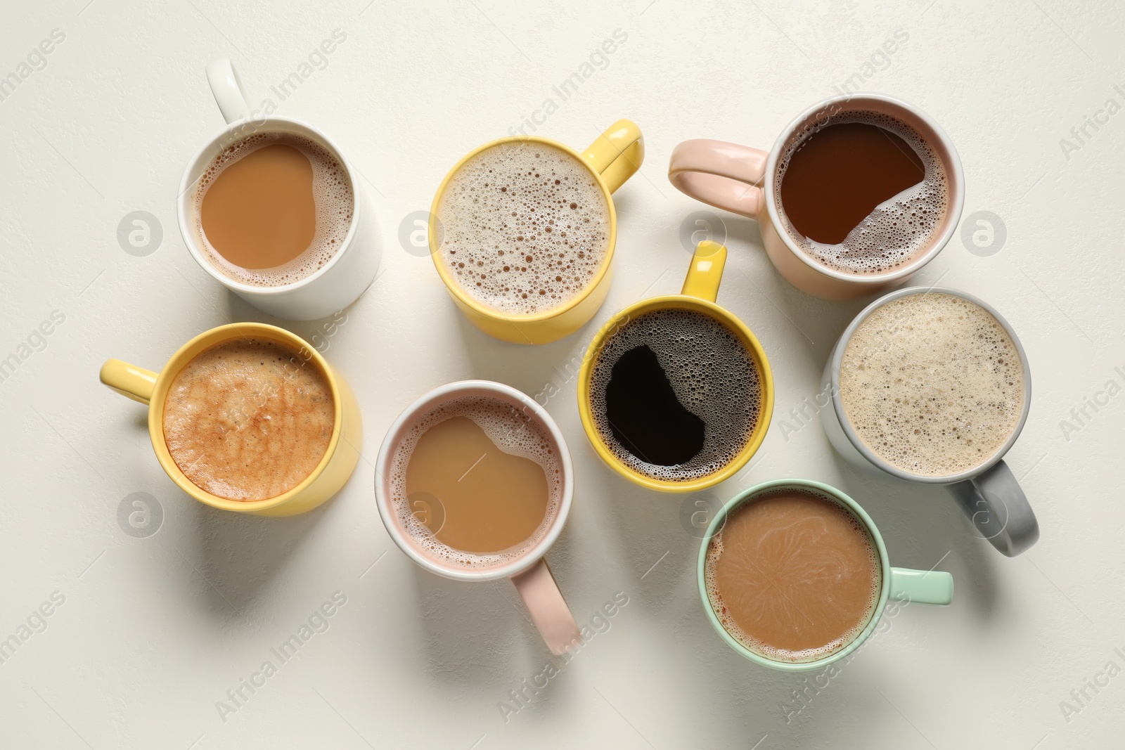 Photo of Many cups with different aromatic coffee on white table, flat lay