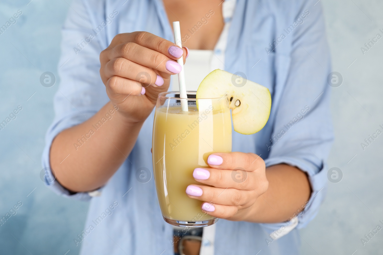 Photo of Woman holding tasty pear juice on light blue background, closeup