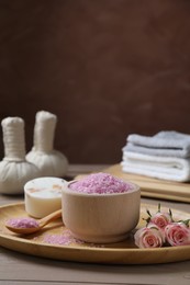 Photo of Bowl of pink sea salt, soap and roses on wooden table. Space for text