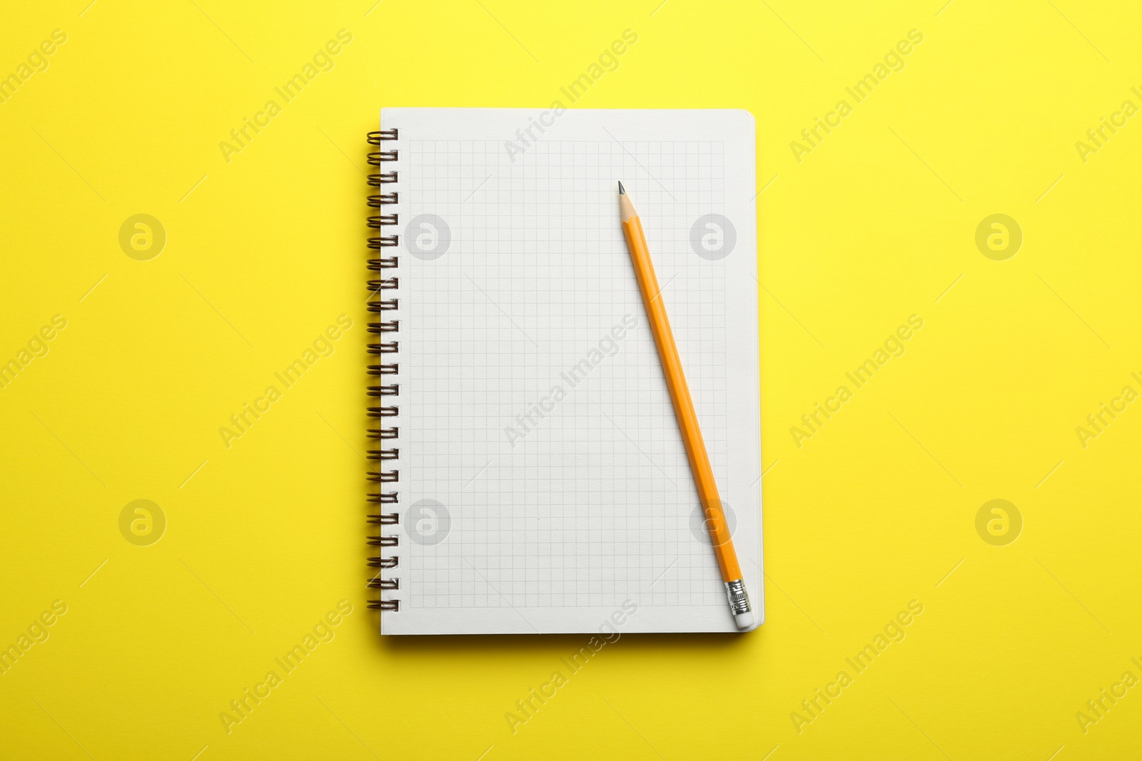 Photo of Notebook and pencil on yellow background, top view