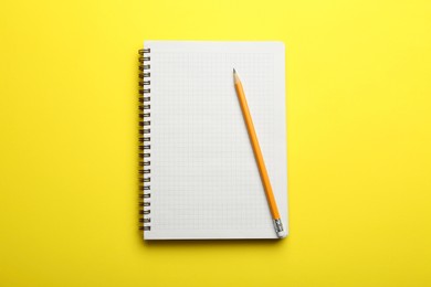 Notebook and pencil on yellow background, top view