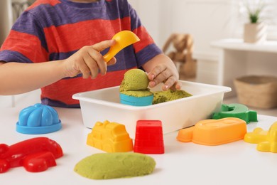 Photo of Little boy playing with bright kinetic sand at table indoors, closeup