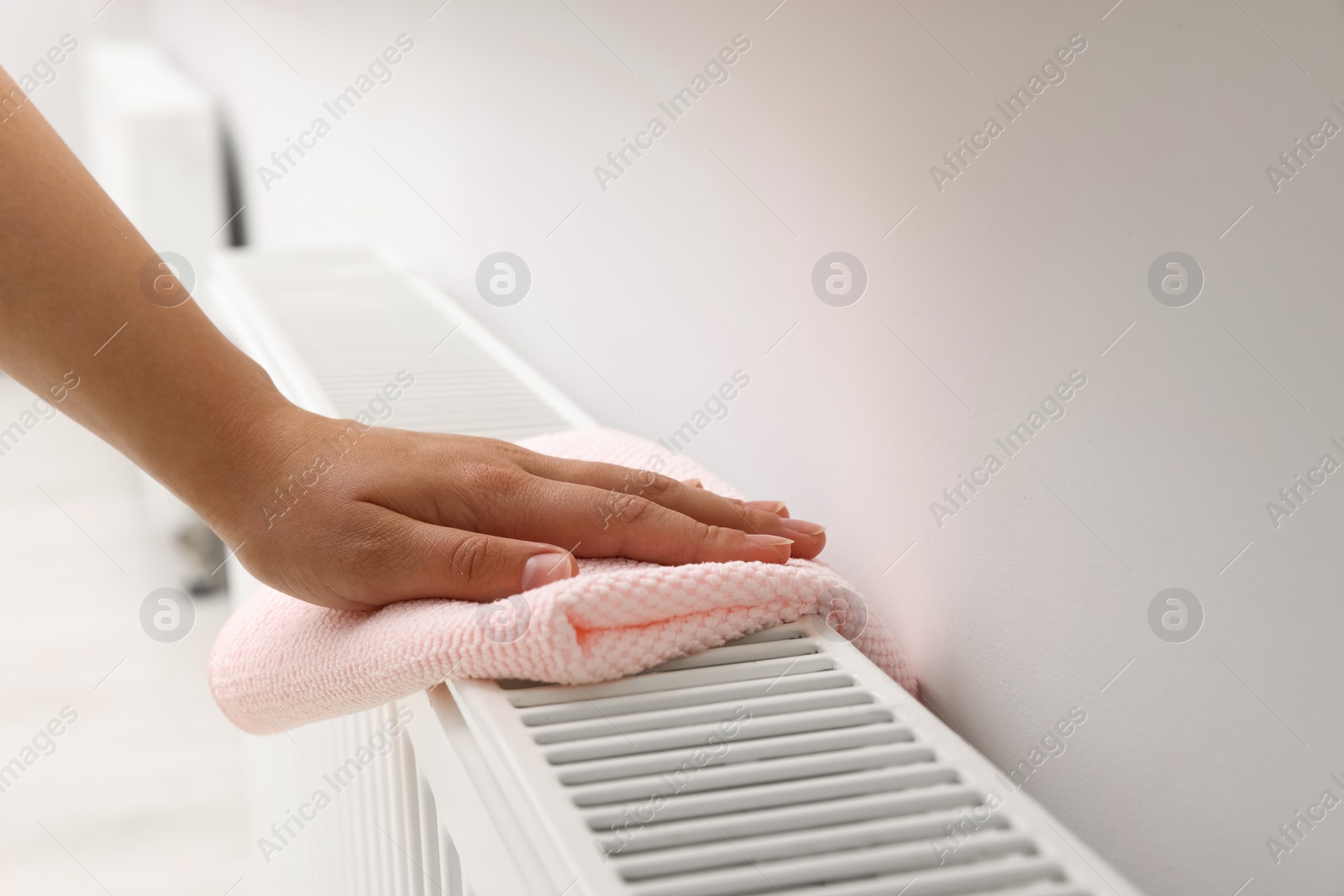 Photo of Woman cleaning radiator with rag indoors, closeup