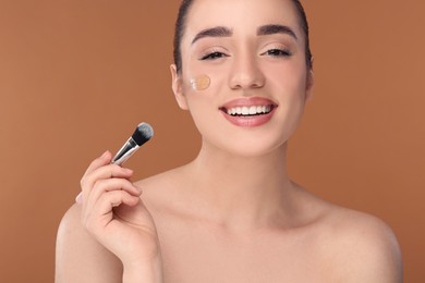 Woman applying foundation on face with brush against brown background