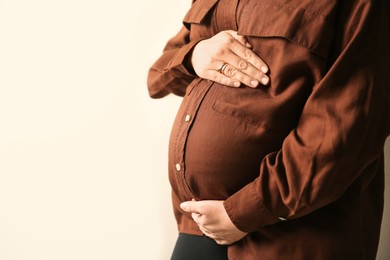 Pregnant woman touching her belly on beige background, closeup. Space for text