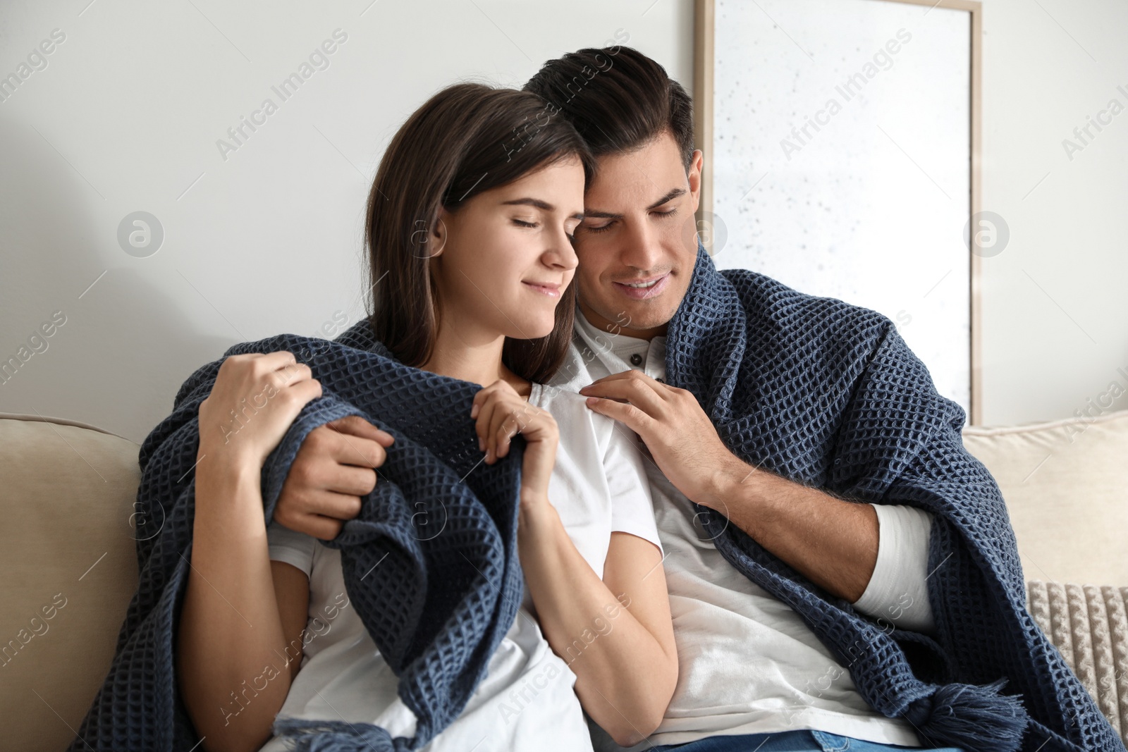 Photo of Happy couple covered with warm dark blue plaid sitting on sofa at home